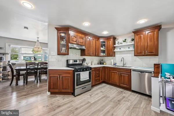 a kitchen with stainless steel appliances granite countertop wooden cabinets a sink a stove a refrigerator and island with wooden floors
