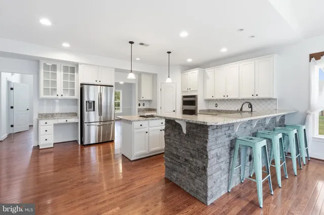 a kitchen with stainless steel appliances granite countertop a refrigerator a stove a sink and white cabinets with wooden floors