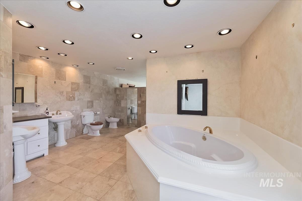 2804 West Sunrise Rim Road Boise, ID 83705 - Photo 42 of 50 Spacious bathroom featuring a built-in soaking tub, recessed ceiling lighting, pedestal sinks, and stone tile flooring