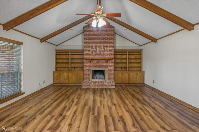 a view of an empty room with wooden floor fireplace and a window