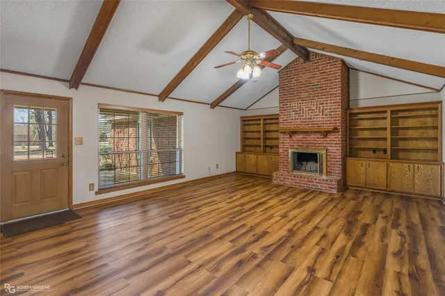 a view of an empty room with wooden floor fireplace and a window