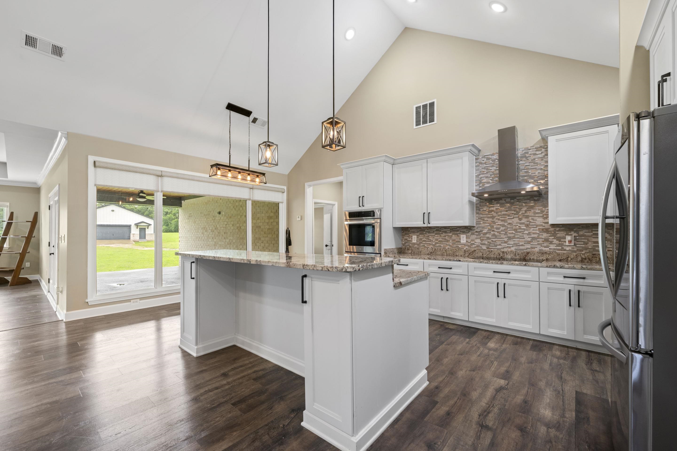 2295 Tomlin Road Somerville, TN 38068 - Photo 10 of 38 Kitchen with appliances with stainless steel finishes, wall chimney range hood, white cabinets, a center island, and tasteful backsplash