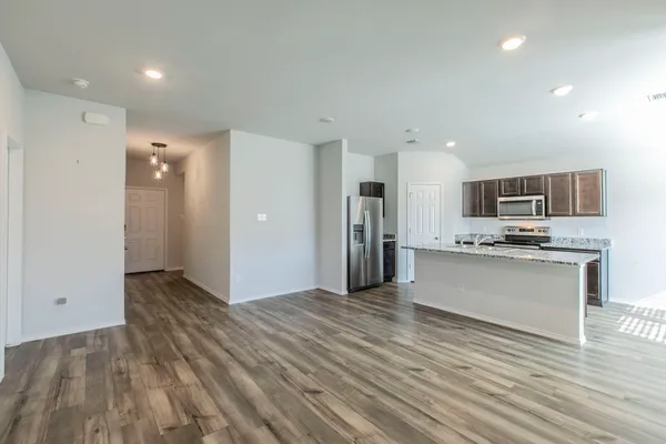 a view of kitchen with kitchen island granite countertop refrigerator oven a sink and white cabinets with wooden floor