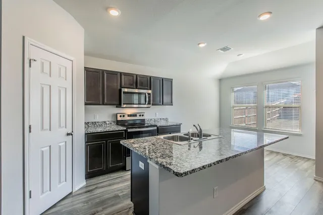 a kitchen with granite countertop kitchen island stainless steel appliances a sink stove refrigerator and cabinets
