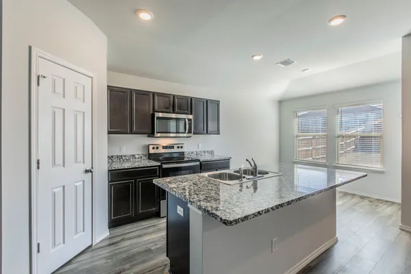 a kitchen with granite countertop kitchen island stainless steel appliances a sink stove refrigerator and cabinets