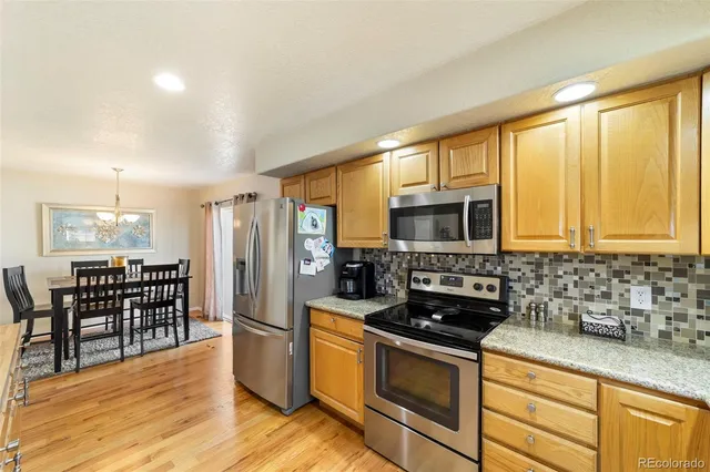 a kitchen with stainless steel appliances granite countertop a stove a sink a refrigerator cabinets and a dining table with wooden floor