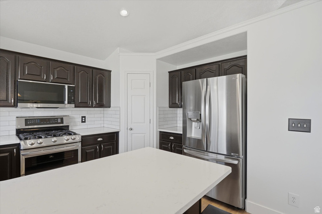 5576 South 4100th Street West Roy, UT 84067 - Photo 10 of 35 Kitchen featuring dark wood cabinetry, stainless steel appliances, white subway tile backsplash, and light-toned countertops