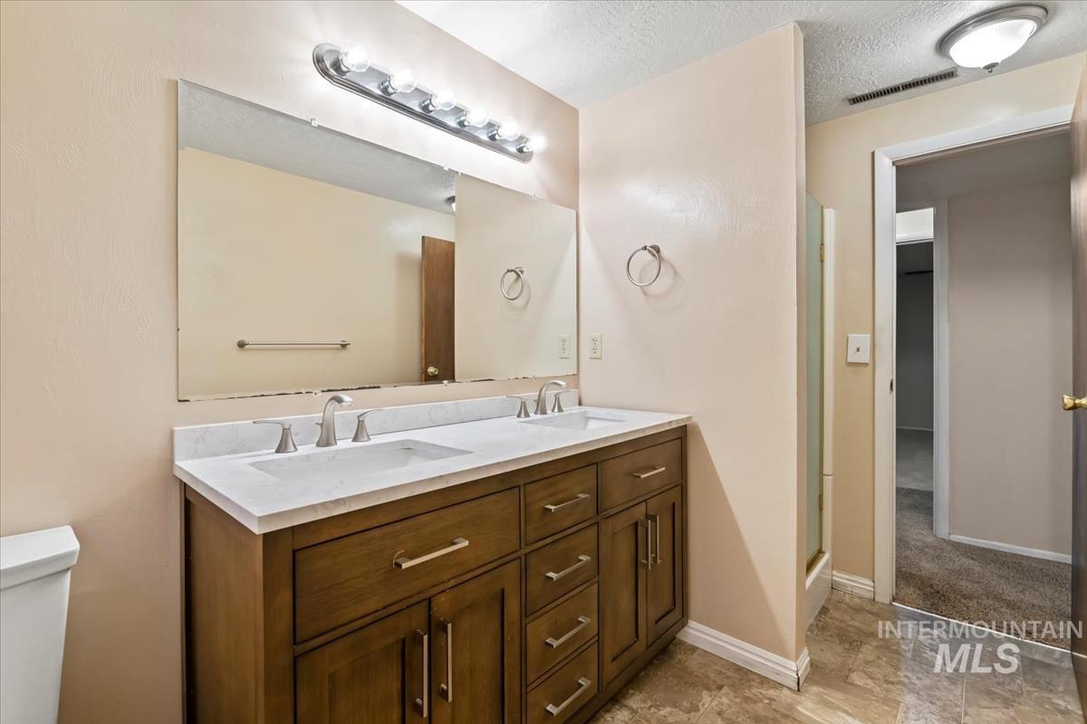 3850 Rugby Drive Boise, ID 83704 - Photo 38 of 44 Bathroom featuring double vanity, a textured ceiling, and a shower with door