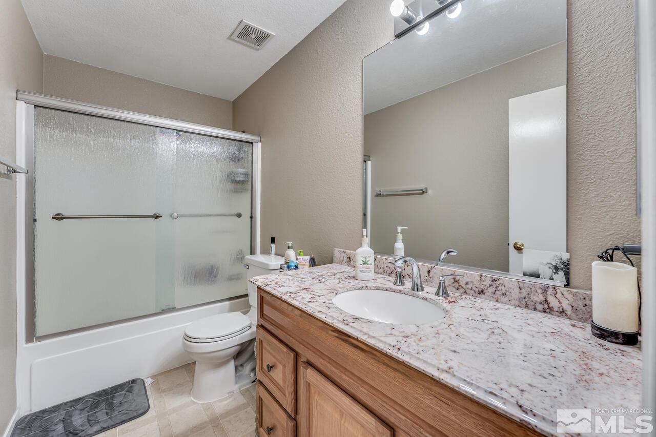 7699 Corso Street Reno, NV 89506 - Photo 24 of 36 a bathroom with a granite countertop sink mirror vanity and toilet