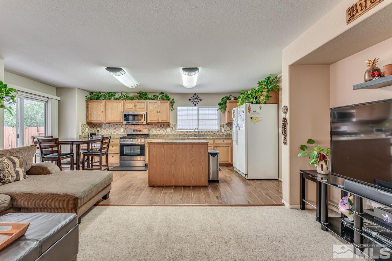 7699 Corso Street Reno, NV 89506 - Photo 7 of 36 a living room with stainless steel appliances kitchen island granite countertop a refrigerator a stove top oven a dining table and chairs