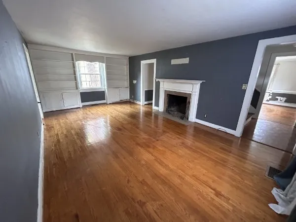 an empty room with wooden floor fireplace and windows