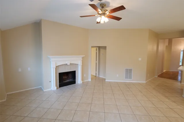 a view of an empty room with chandelier fan and fire place