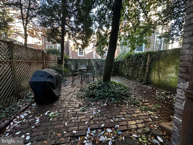 a view of a backyard with table and chairs potted plants and large tree
