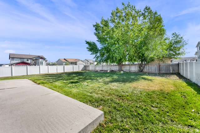 2575 Athena Drive Magna, UT 84044 - Photo 23 of 23 Spacious backyard featuring a large concrete patio, mature trees, and a combination of white vinyl and wood fencing