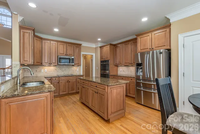 a kitchen with stainless steel appliances granite countertop a stove top oven a refrigerator a sink and dishwasher with wooden floor