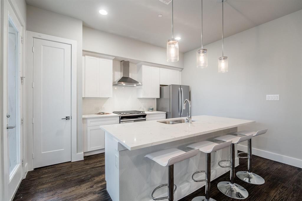 770 North Plano Road, Unit 303 Richardson, TX 75081 - Photo 5 of 26 Kitchen with dark hardwood flooring, white cabinetry, a stainless steel range hood, and a kitchen island with a sink and pendant lighting