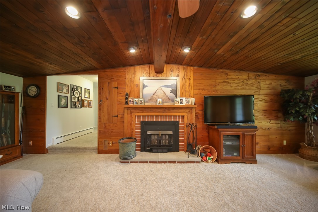 3362 Granger Road Medina, OH 44256 - Photo 6 of 49 Carpeted living room featuring a fireplace, a baseboard heating unit, wood ceiling, wooden walls, and lofted ceiling