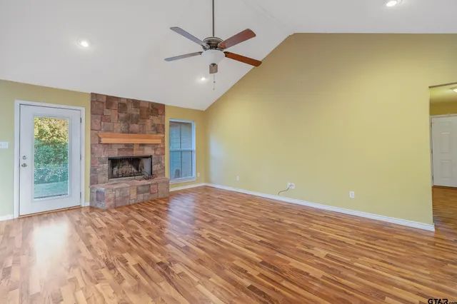 an empty room with wooden floor a fireplace and a ceiling fan