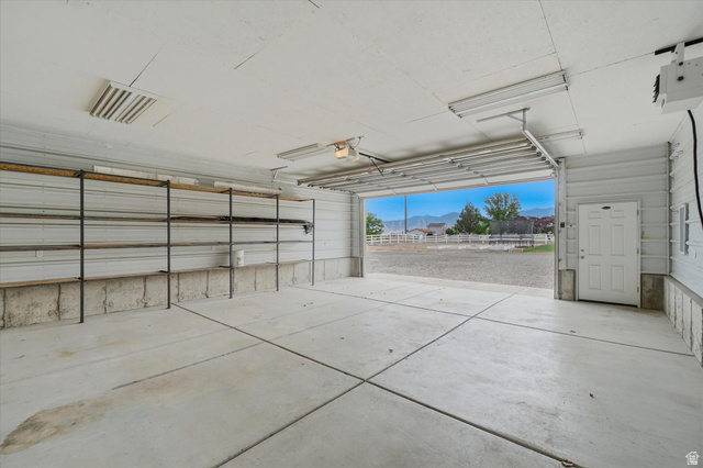 791 East Saddle Road Grantsville, UT 84029 - Photo 45 of 46 Spacious garage featuring a concrete floor, built-in shelving, an overhead garage door, a side entry door, and fluorescent lighting
