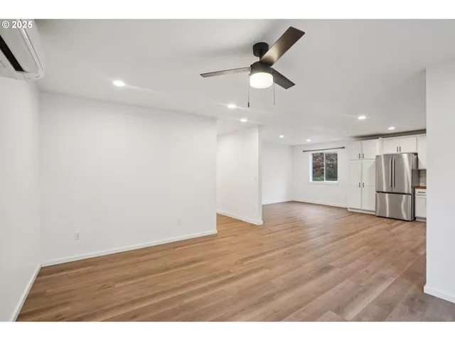 a view of an empty room with wooden floor and a ceiling fan