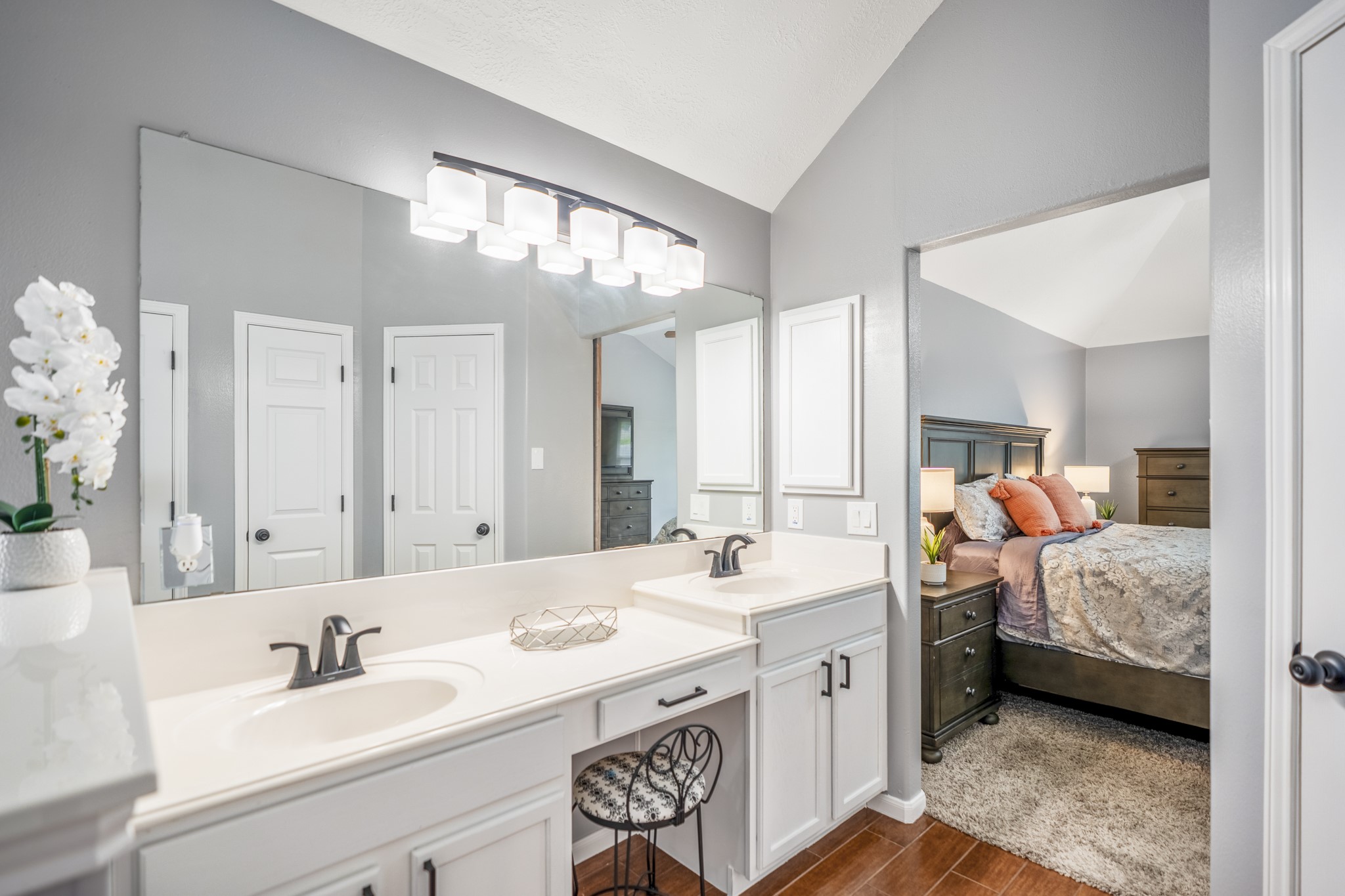 3411 Utah Beach Court Spring, TX 77388 - Photo 26 of 50 Primary bath storage and function come together along this extended dual-sink vanity, with a seated makeup area positioned between the sinks and bright lighting stretching across the mirrors. The doorway on the right looks back into the primary bedroom, keeping the suite connected while giving the bath its own defined space.
