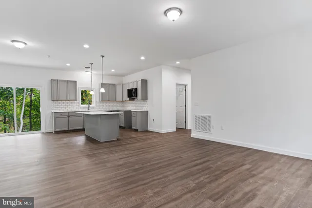 a large white kitchen with stainless steel appliances kitchen island a stove a sink dishwasher and a refrigerator with wooden floor