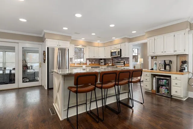 a kitchen with granite countertop a stove a sink and white cabinets with wooden floor next to windows