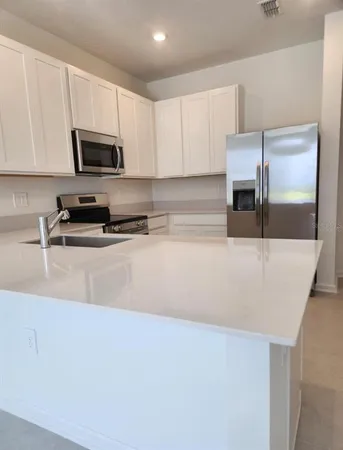 a kitchen with stainless steel appliances a sink a stove a microwave a refrigerator a sink and white cabinets