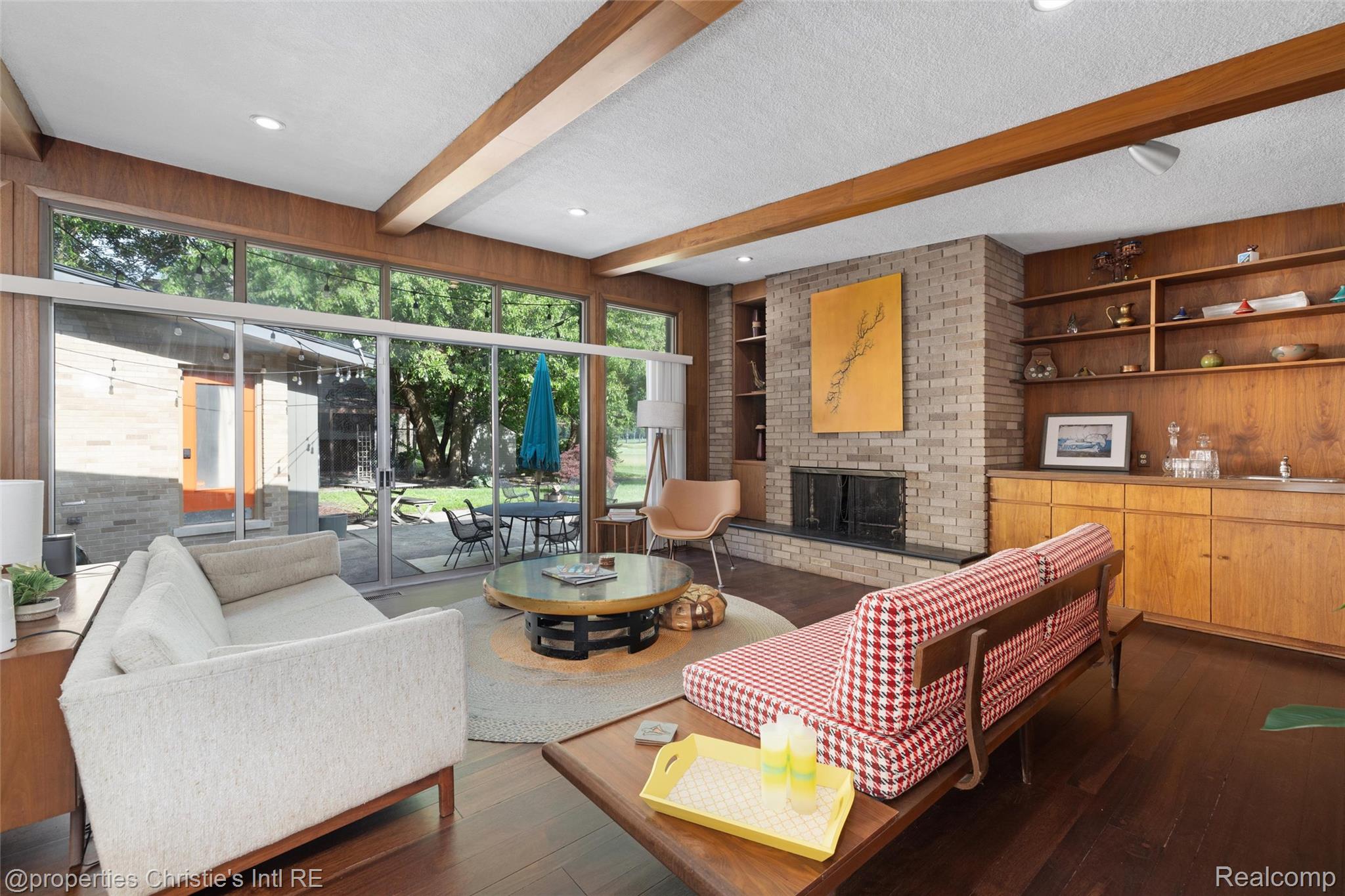 2771 West Seven Mile Road Detroit, MI 48221 - Photo 4 of 57 Living area featuring extensive full-height windows, a brick fireplace, wood-beam ceiling accents, built-in shelving, and rich wood-finish flooring