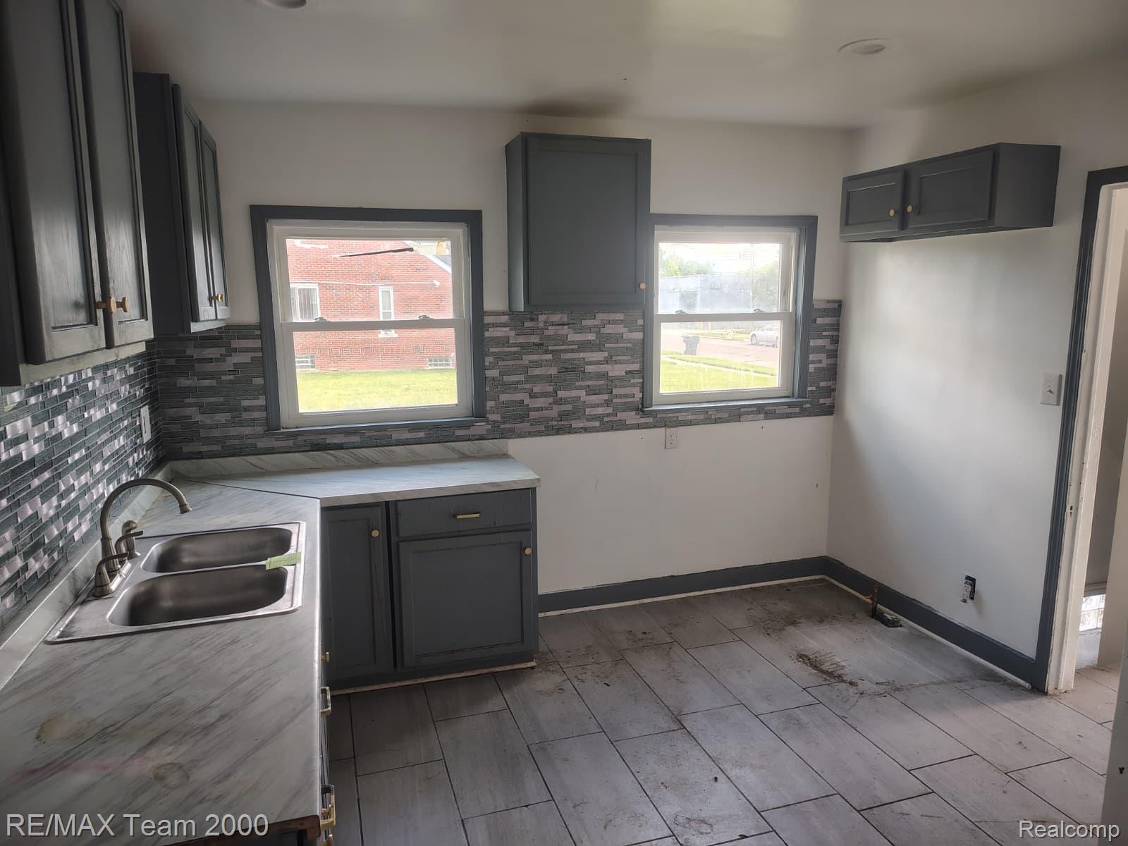 8860 Appoline Street Detroit, MI 48228 - Photo 9 of 45 Kitchen featuring grey cabinetry, a stainless steel double-basin sink, patterned tile backsplash, and light-toned countertops