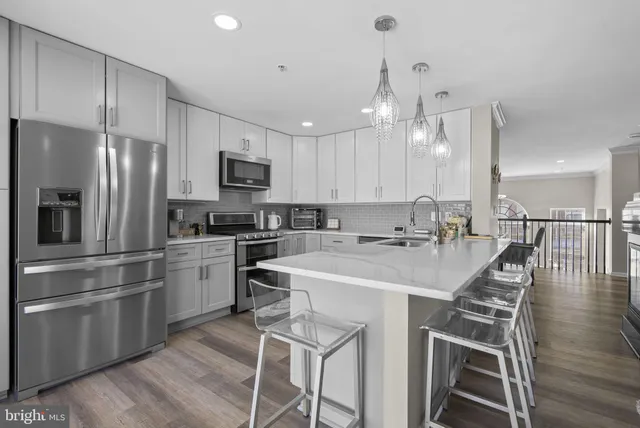 a kitchen with stainless steel appliances kitchen island granite countertop a sink a stove a refrigerator and island with wooden floor