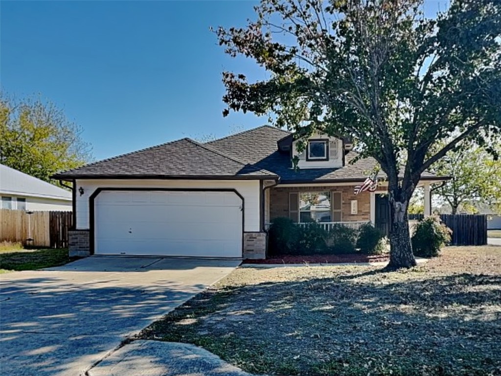 View of front of property featuring driveway, a porch, a garage, brick siding, and roof with shingles