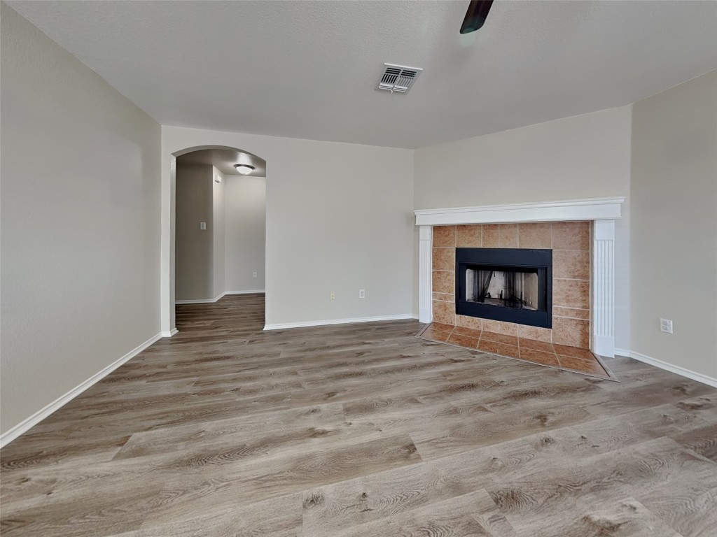 228 Fall Creek Drive Kyle, TX 78640 - Photo 3 of 19 Unfurnished living room with arched walkways, a ceiling fan, light wood-style flooring, and a tile fireplace