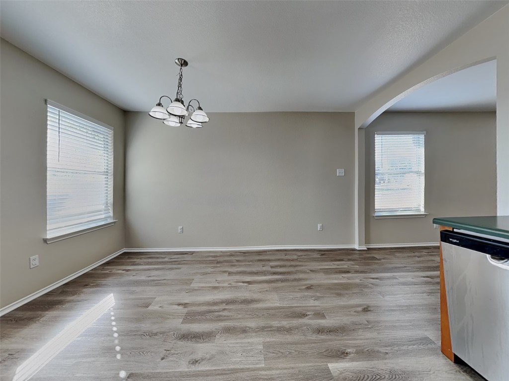 228 Fall Creek Drive Kyle, TX 78640 - Photo 4 of 19 Unfurnished dining area featuring light wood-type flooring, a chandelier, arched walkways, and healthy amount of natural light