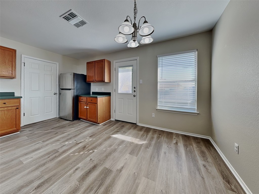 228 Fall Creek Drive Kyle, TX 78640 - Photo 5 of 19 Kitchen with dark countertops, brown cabinets, decorative light fixtures, freestanding refrigerator, and a chandelier