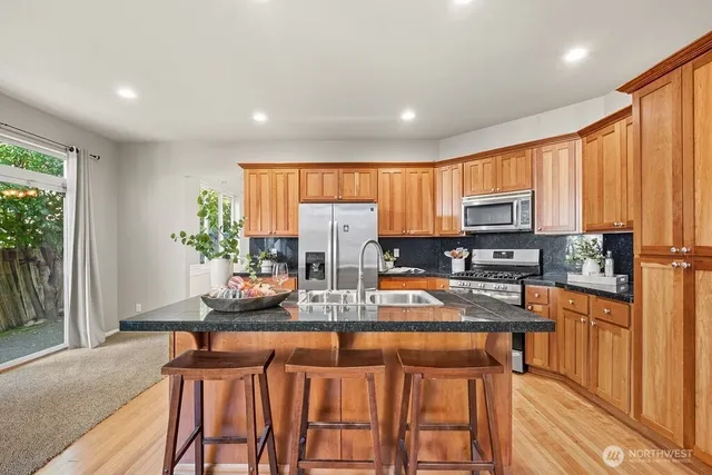 a kitchen with stainless steel appliances granite countertop a stove top oven a sink dishwasher and a refrigerator with wooden floor