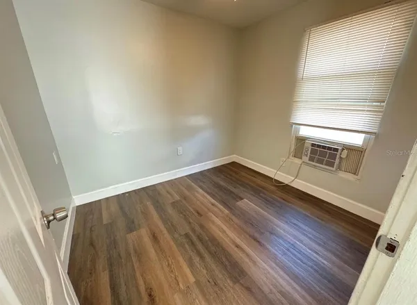 a view of an empty room with wooden floor and window