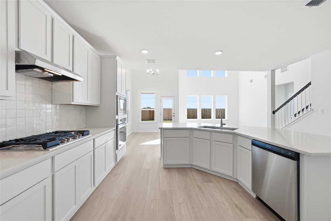 205 Caraway Drive Taylor, TX 76574 - Photo 4 of 15 Kitchen with appliances with stainless steel finishes, light wood-style flooring, white cabinetry, decorative backsplash, and under cabinet range hood