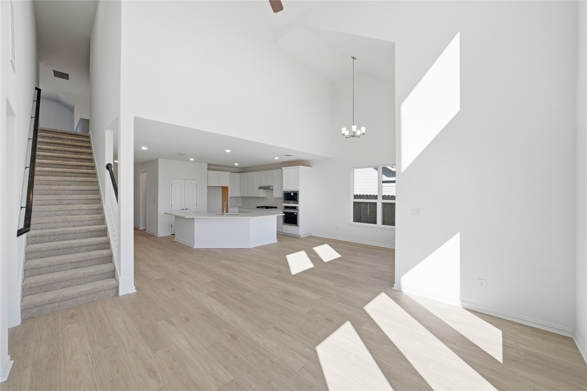 205 Caraway Drive Taylor, TX 76574 - Photo 6 of 15 Unfurnished living room with stairs, a towering ceiling, light wood-style flooring, a chandelier, and recessed lighting