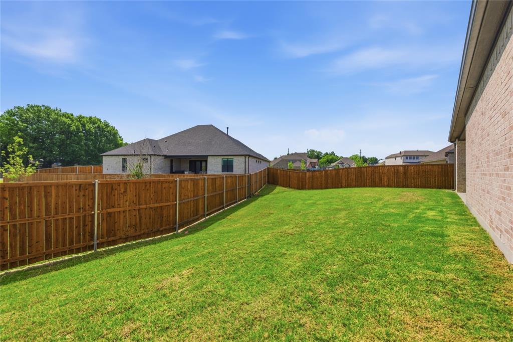 709 Anne Road Van Alstyne, TX 75495 - Photo 27 of 28 Expansive backyard featuring a green lawn, wood privacy fencing, and a visible portion of the property's brick exterior