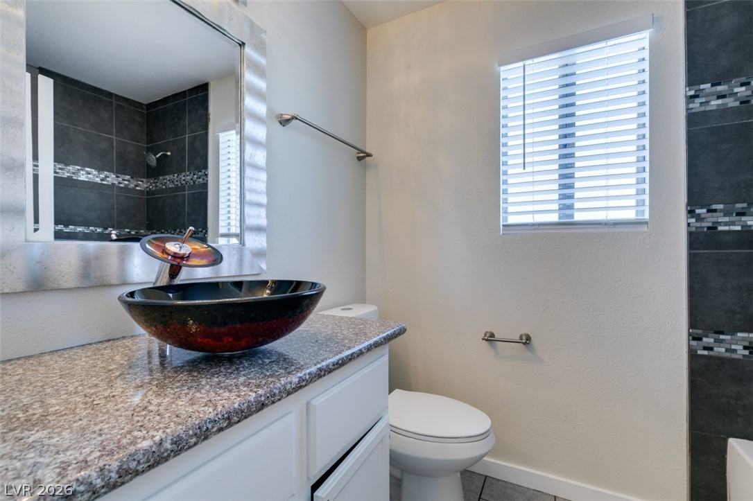 2028 Rustler Ridge Avenue North Las Vegas, NV 89031 - Photo 27 of 40 A stylish bathroom features a granite counter with a distinctive vessel sink and a tiled shower reflected in the mirror.