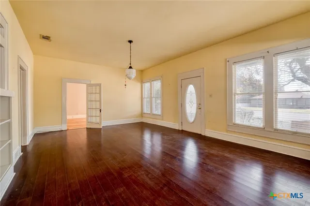 a view of an empty room with wooden floor and a window