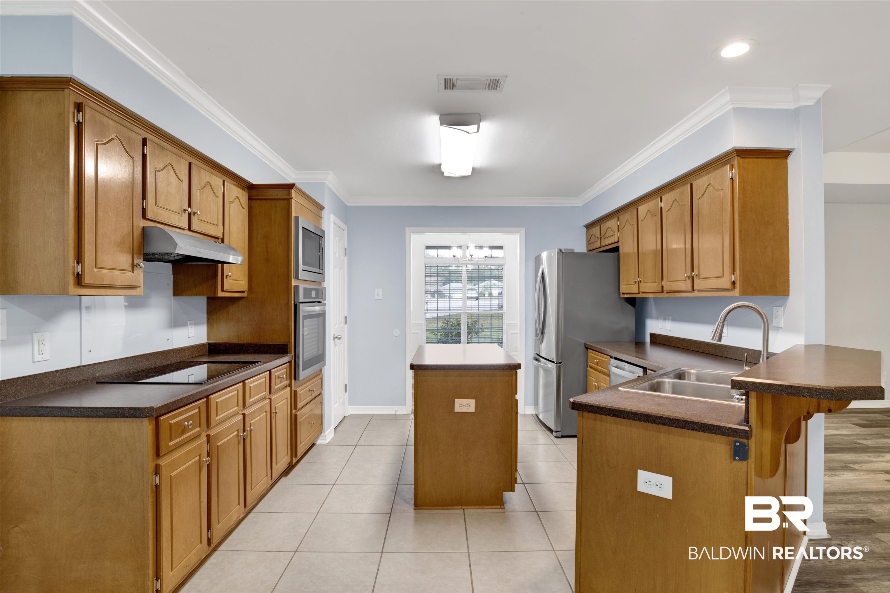 9534 Labrador Run North Mobile, AL 36695 - Photo 7 of 30 Kitchen with crown molding, brown cabinets, dark countertops, light tile patterned floors, and a kitchen island
