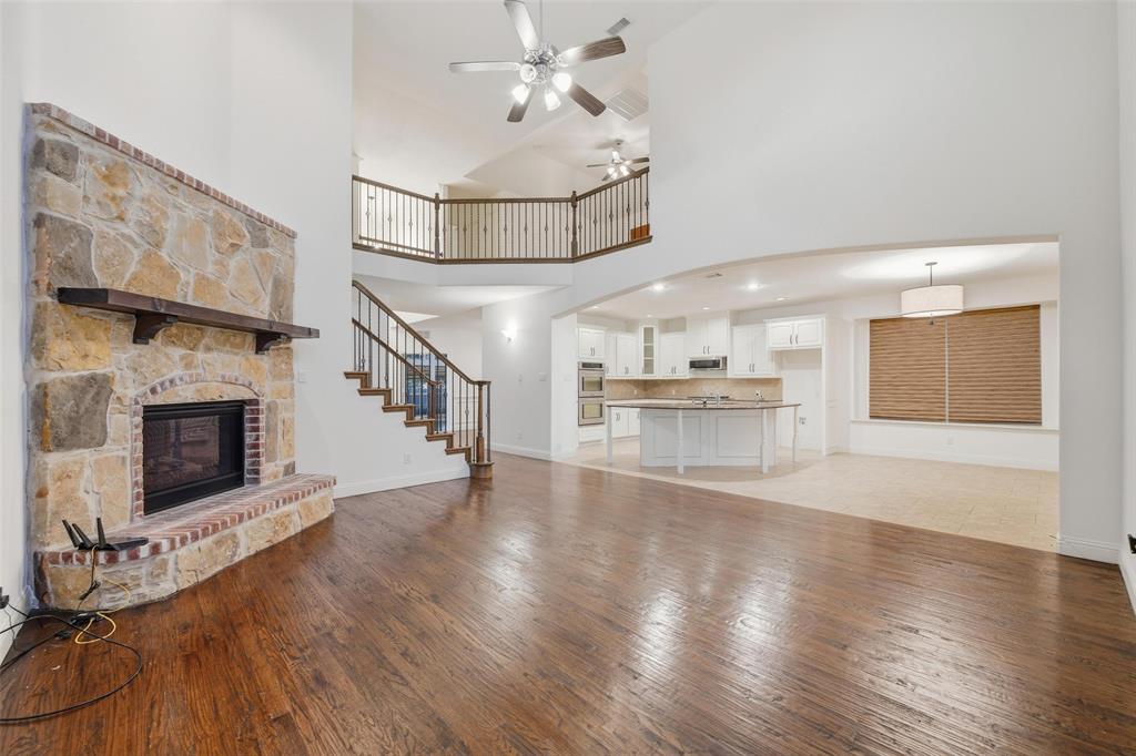 1321 Talley Lane Frisco, TX 75033 - Photo 7 of 40 Unfurnished living room featuring light wood-style flooring, a fireplace, stairway, a ceiling fan, and a towering ceiling