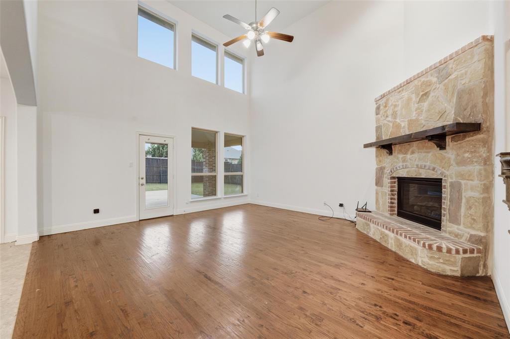 1321 Talley Lane Frisco, TX 75033 - Photo 9 of 40 Unfurnished living room with wood finished floors, plenty of natural light, a stone fireplace, and a towering ceiling