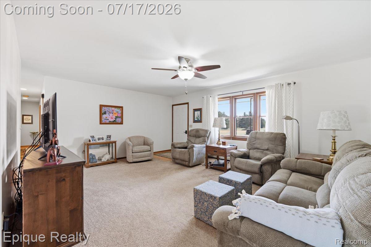 555 East Square Lake Road Troy, MI 48085 - Photo 10 of 48 Bright living space featuring a ceiling fan with integrated lighting, large window with outdoor scenery, and neutral carpeting