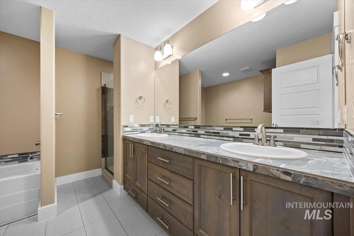 13557 Signorello Street Caldwell, ID 83607 - Photo 19 of 30 Full bath featuring backsplash, double vanity, light tile patterned flooring, a shower stall, and a garden tub