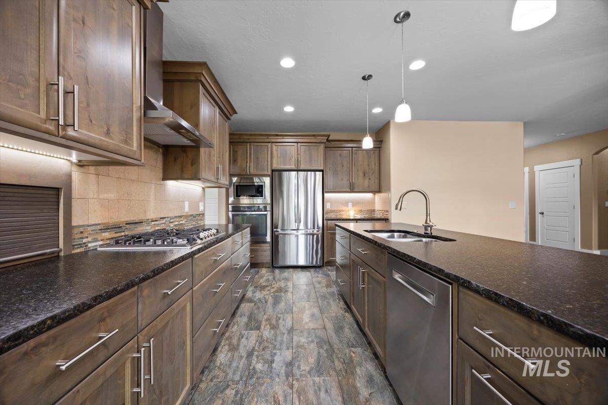 13557 Signorello Street Caldwell, ID 83607 - Photo 7 of 30 Kitchen with tasteful backsplash, stainless steel appliances, wall chimney exhaust hood, recessed lighting, and decorative light fixtures