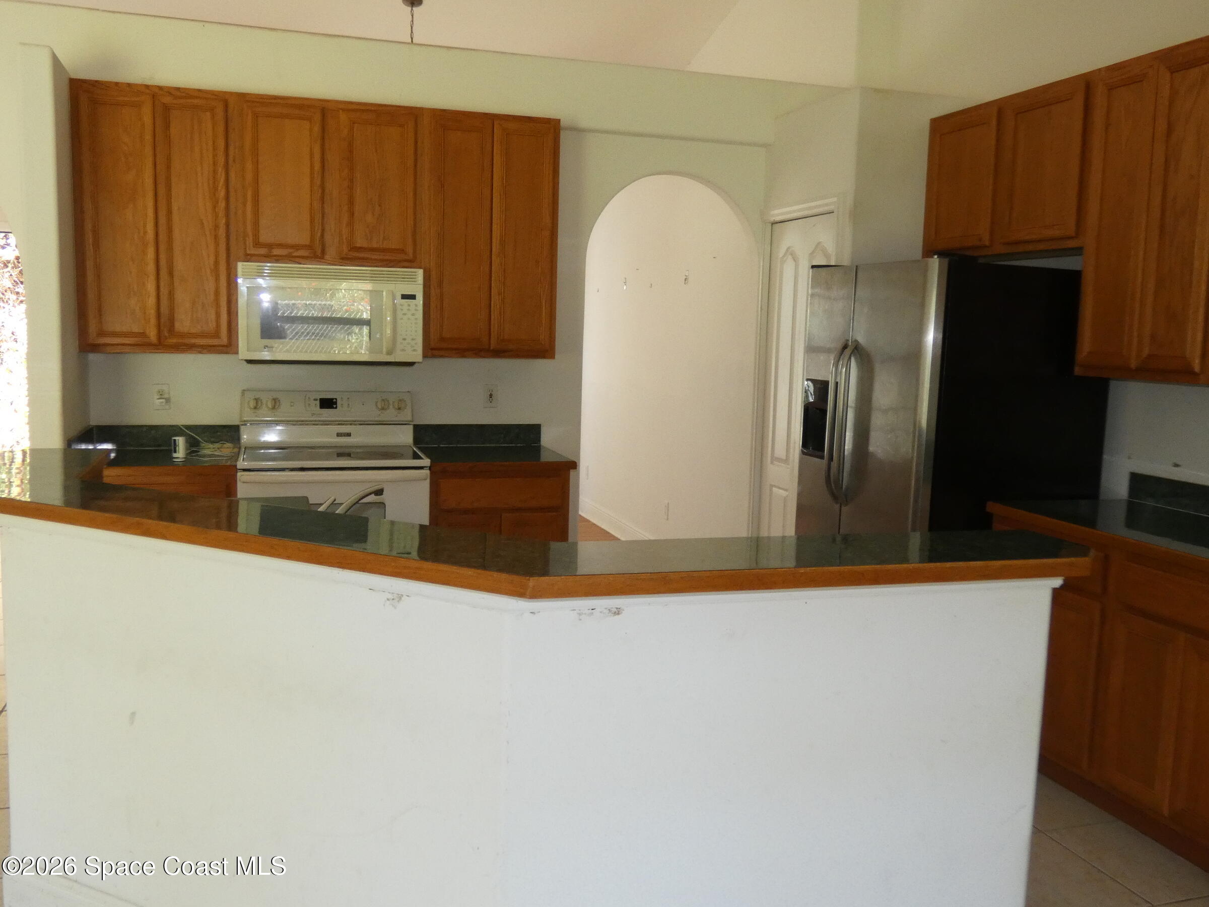 3195 Legendary Lane Melbourne, FL 32935 - Photo 4 of 25 a kitchen with stainless steel appliances granite countertop a refrigerator a stove and a sink with wooden cabinets