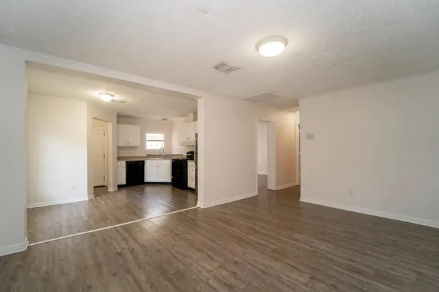 a view of an empty room with wooden floor and kitchen
